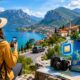 Traveler with a backpack using a smartphone on a mountain viewpoint overlooking a lake, winding road, and European village during an outdoor adventure.