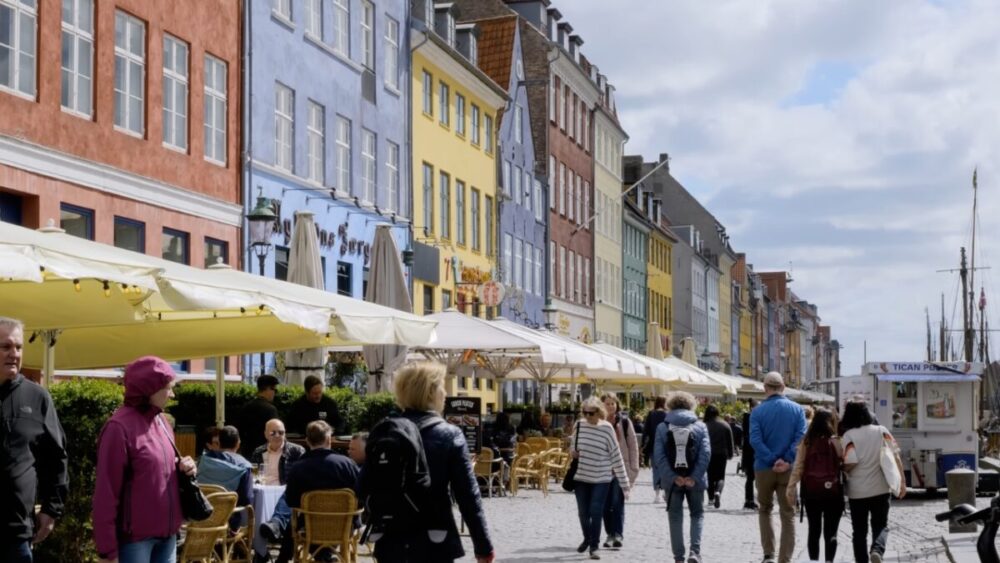 People stroll past colourful houses and outdoor cafés along Copenhagen’s Nyhavn waterfront