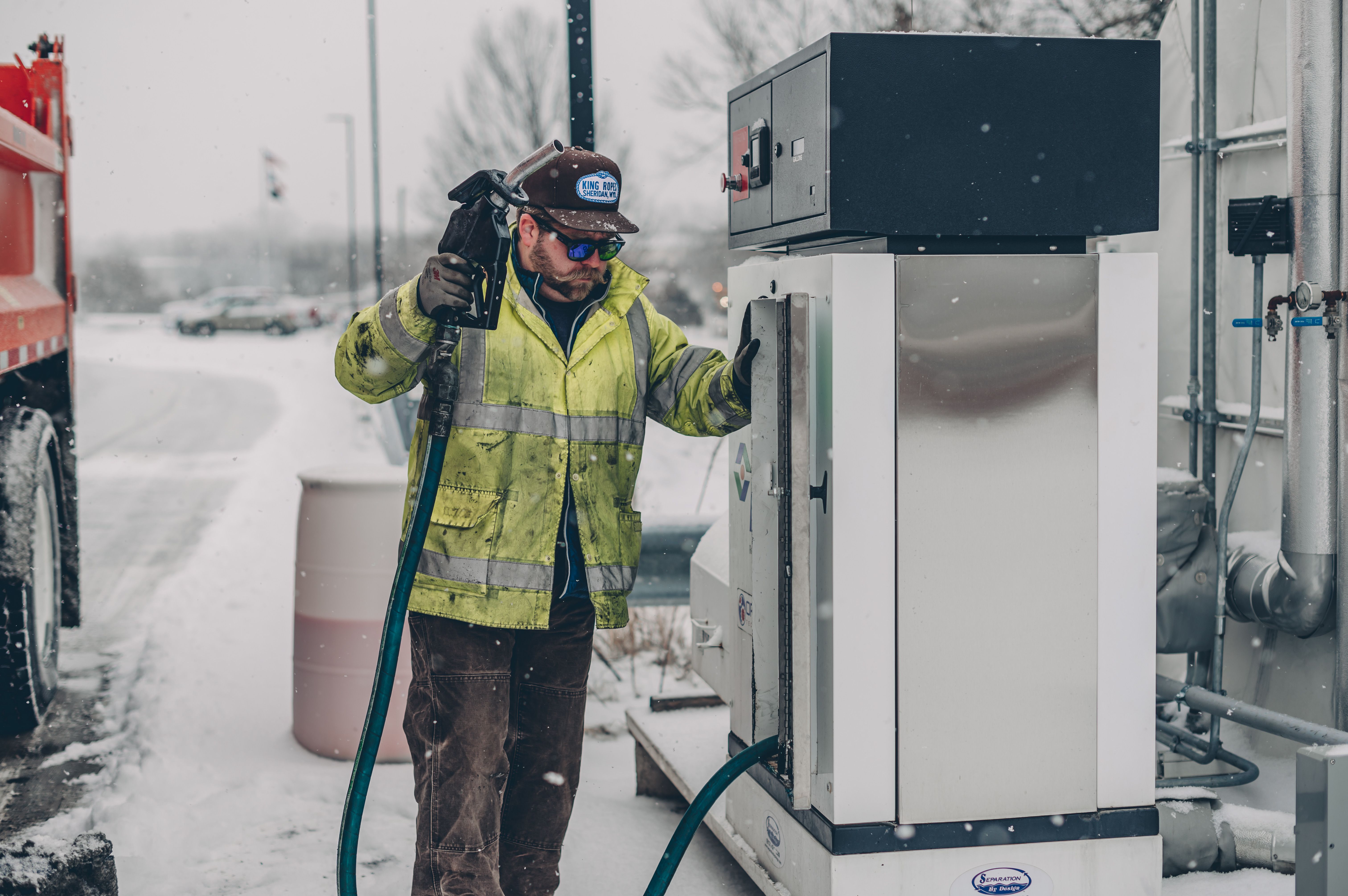 Driver refueling a truck with diesel at a gas station during winter snowfall