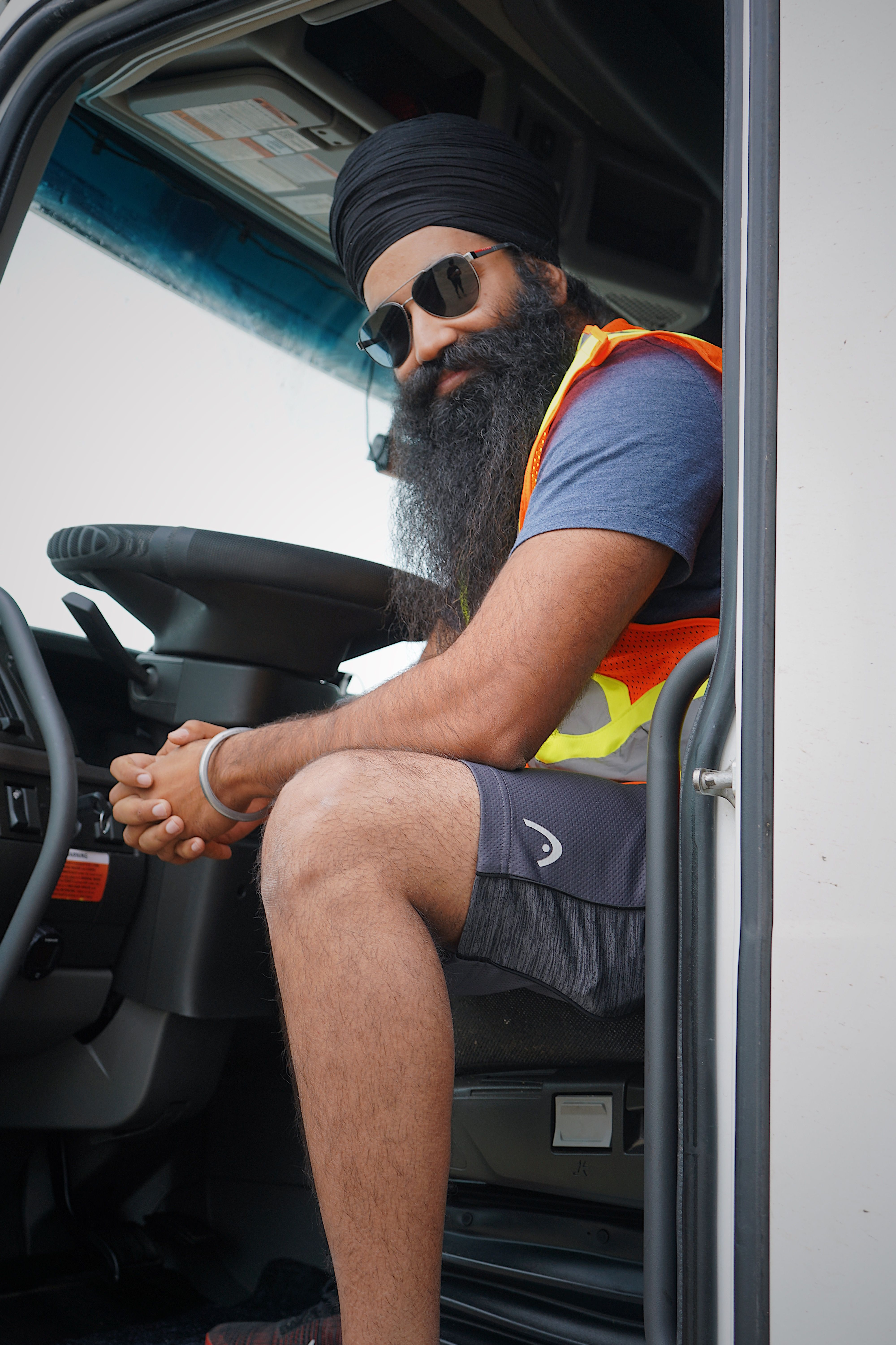 Bearded truck driver wearing sunglasses and a safety vest posing confidently in his truck
