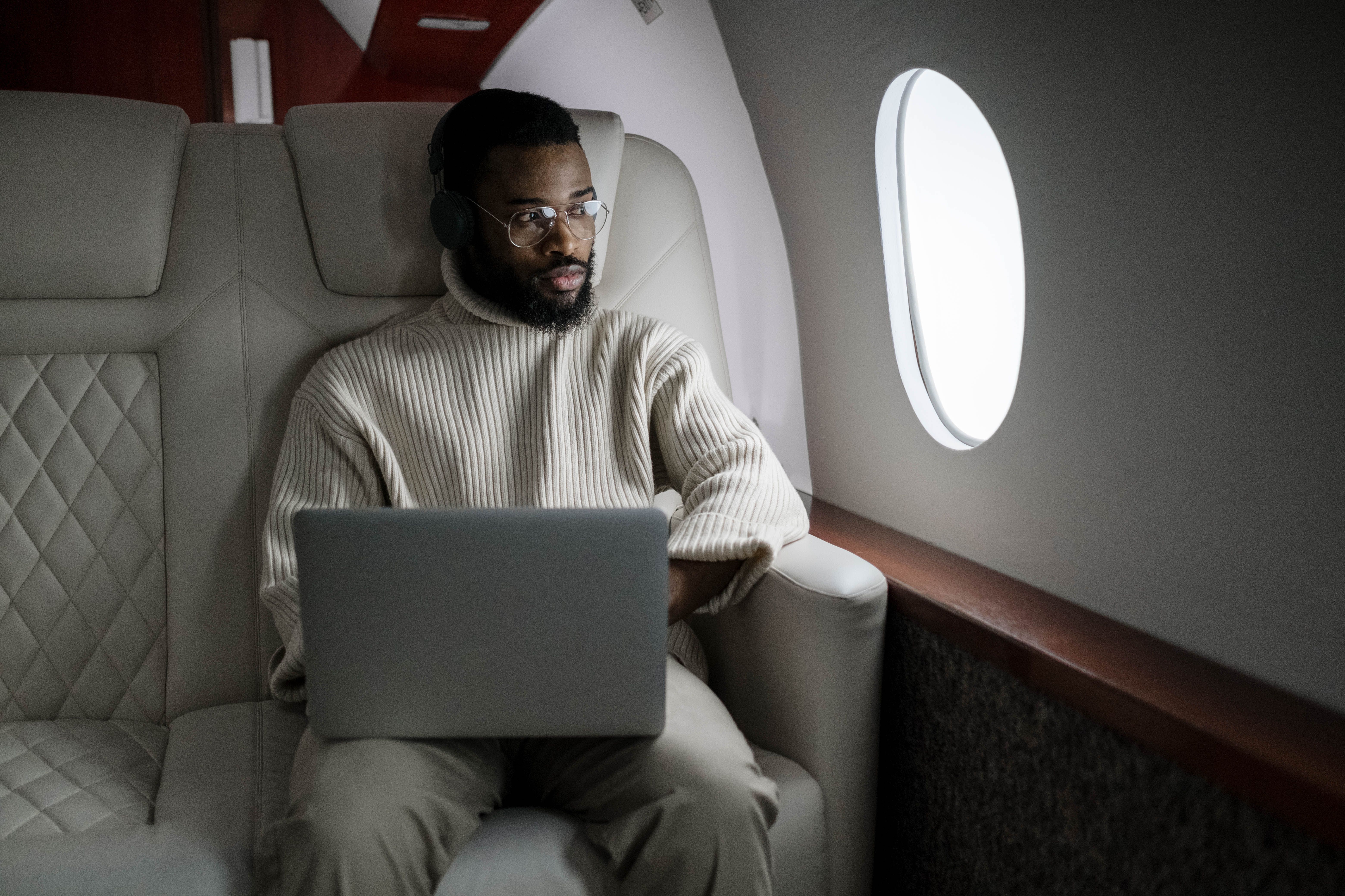 Businessman wearing headphones working on a laptop aboard an airplane cabin
