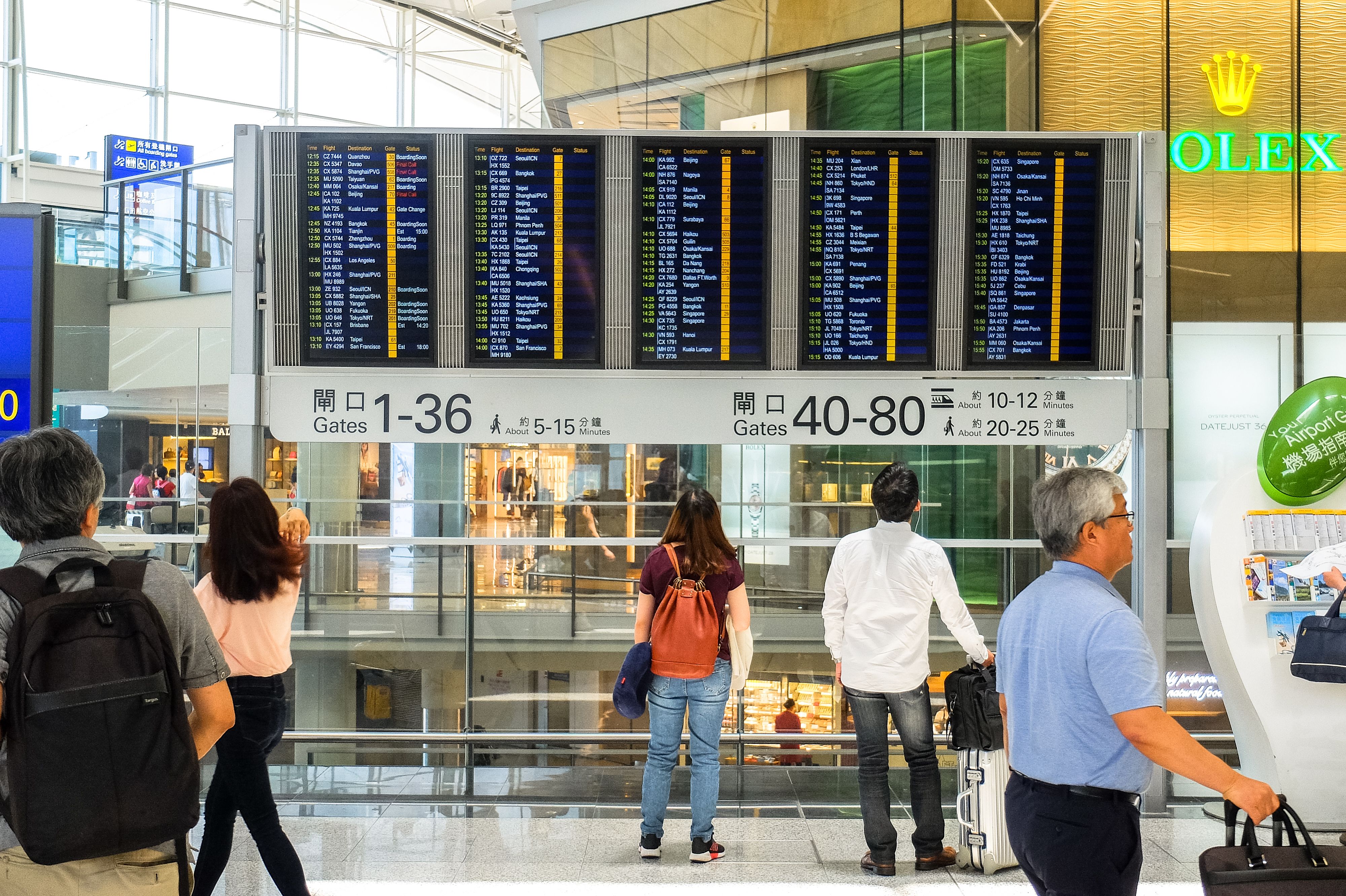 Travelers checking a departure board in an airport terminal, comparing flight options and connections.